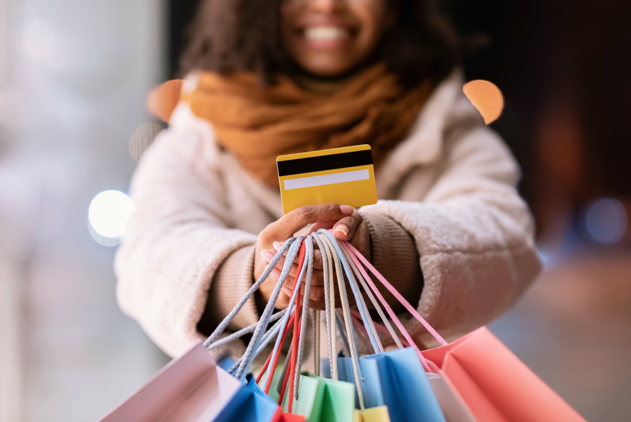 Black woman holding a debit card while also holding giftbags for the holidays.