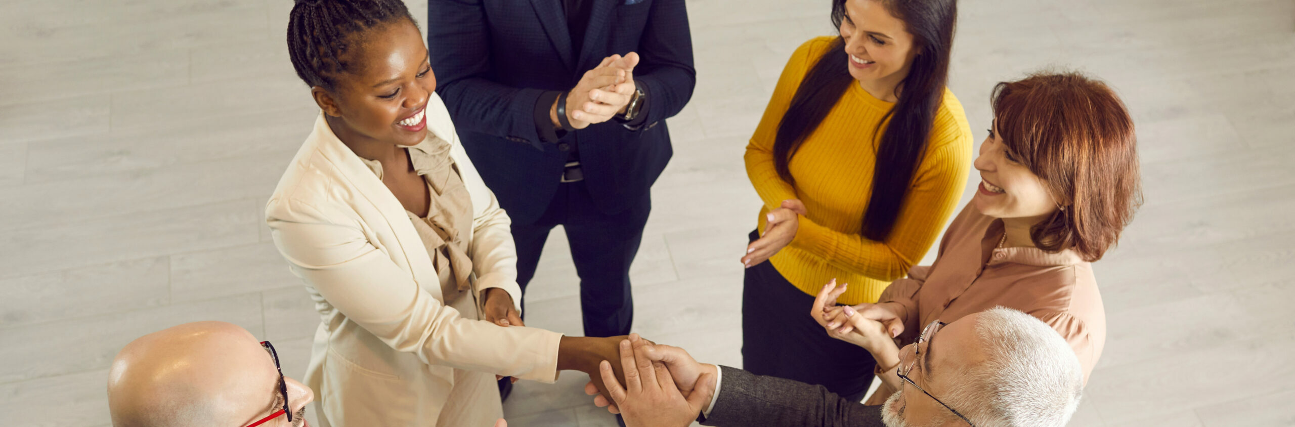 Group of cheerful positive diverse multiethnic people meeting and getting acquainted at casual business event. Young black woman feeling at ease and exchanging handshake with senior man. High angle